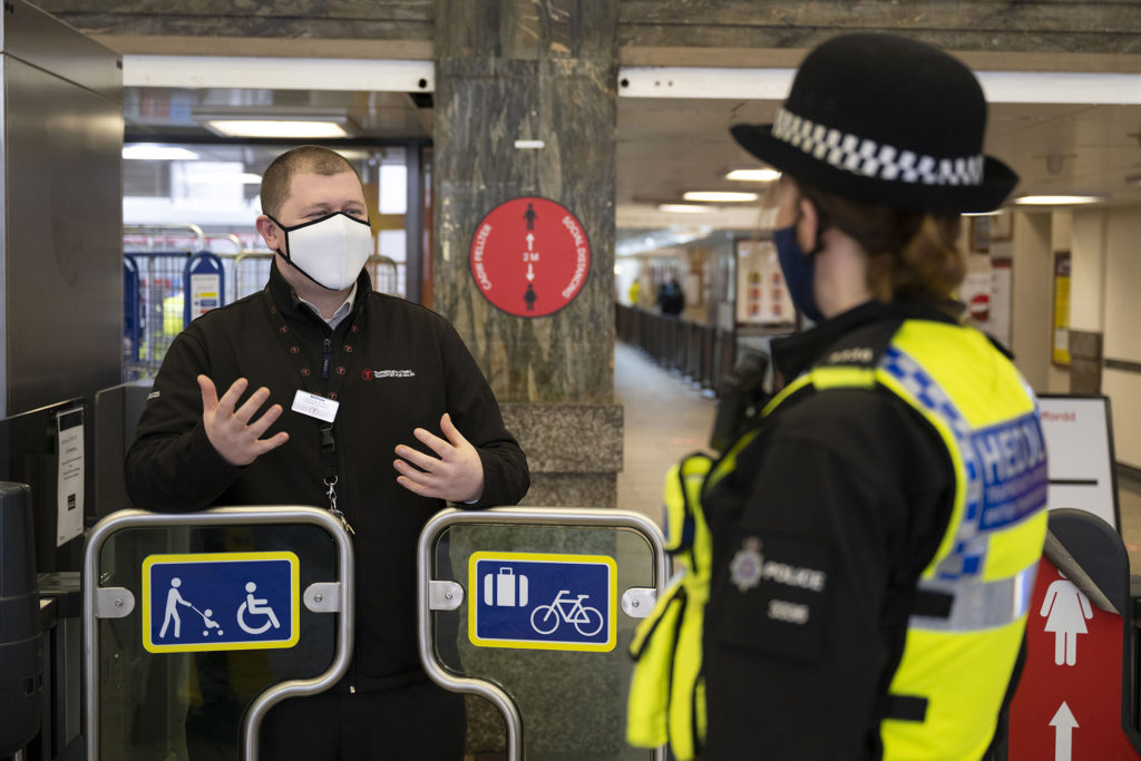 A police officer and railway worker chatting whilst wearing face masks on.
