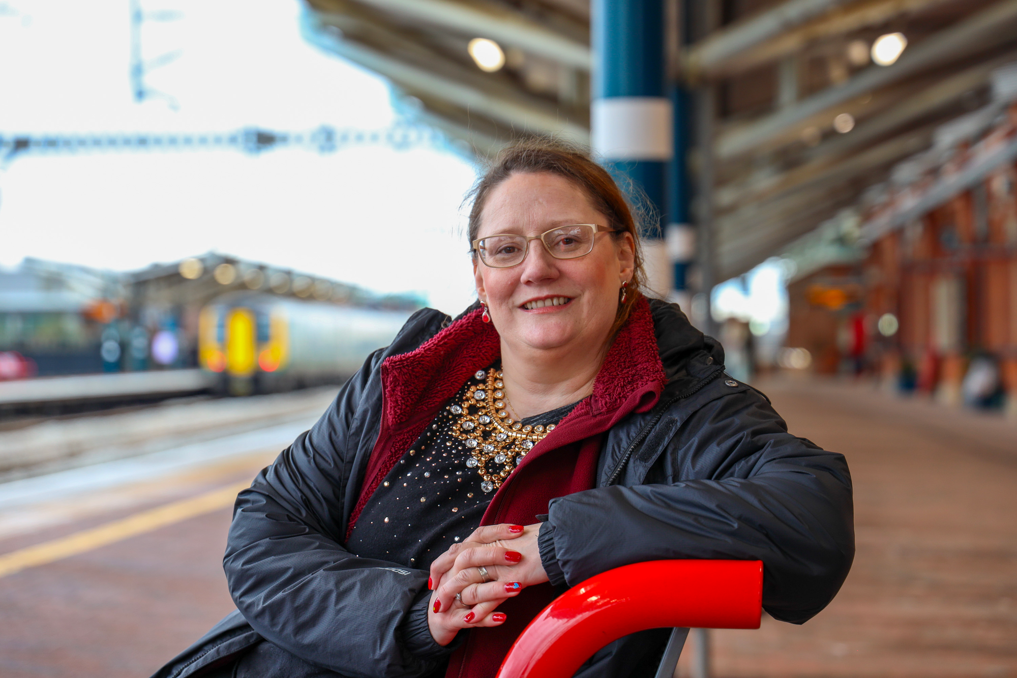 Chaplain Karen, pictured smiling at the camera whilst sitting on a platform bench.