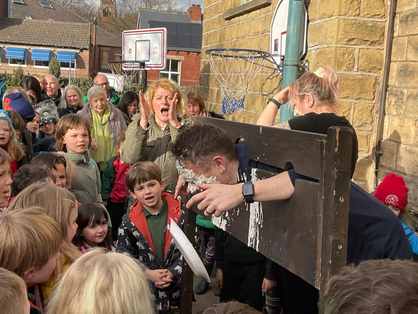 Mr.Barnes, trapped inside a pillory, as pupils launch their attach with custard pies.