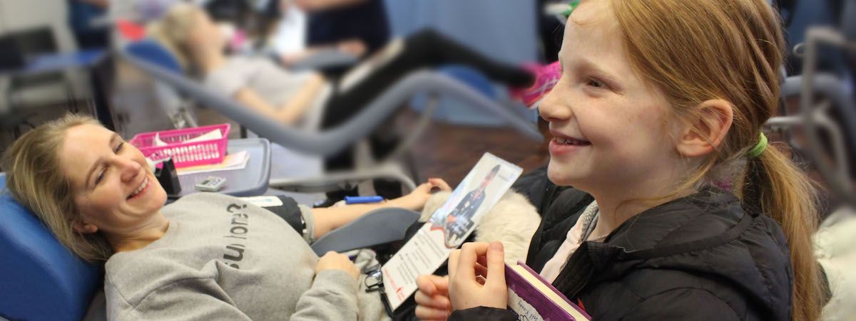 A lady laid down giving blood with a child by her side.